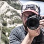 Fotograf im Portrait von vorne, mit einem Objektiv vor dem Gesicht